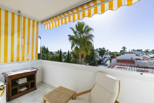 Sunny terrace with yellow striped awning overlooking Marbella gardens and palm trees at Royal Gardens apartment