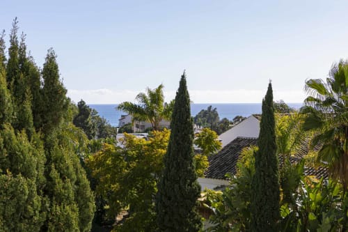 Marbella apartment terrace view with cypress trees, Mediterranean sea, and coastal homes in Nueva Andalucía