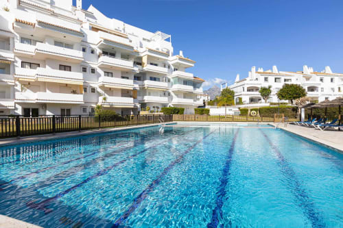 Crystal-clear swimming pool with lane markings at Marbella Home Rentals, surrounded by white apartment buildings in Nueva