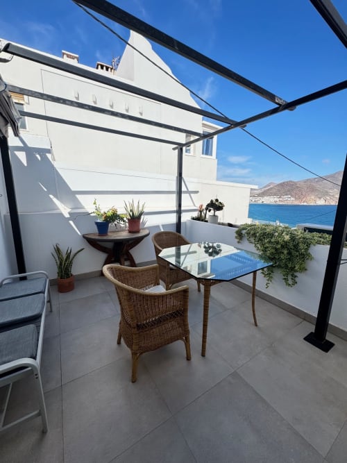 Soleada terraza con vistas al mar en El Faro De Los Genoveses con sillas de mimbre, mesa de comedor y vista a la costa mediterránea.