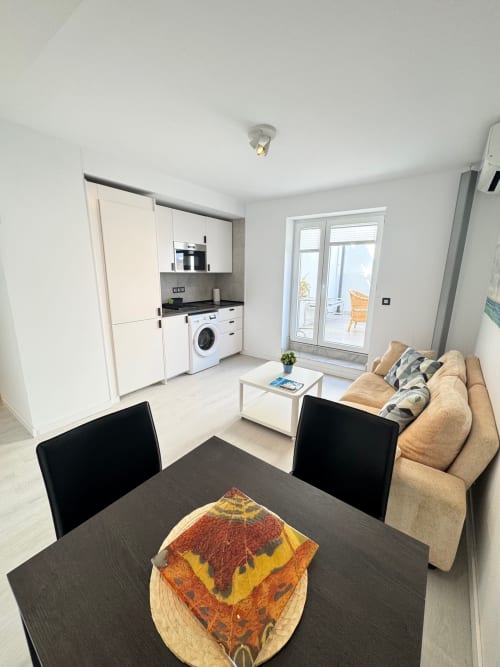 Apartamento estudio moderno en San José, Almería con cocina abierta, comedor, sofá y acceso a balcón con vistas al mar