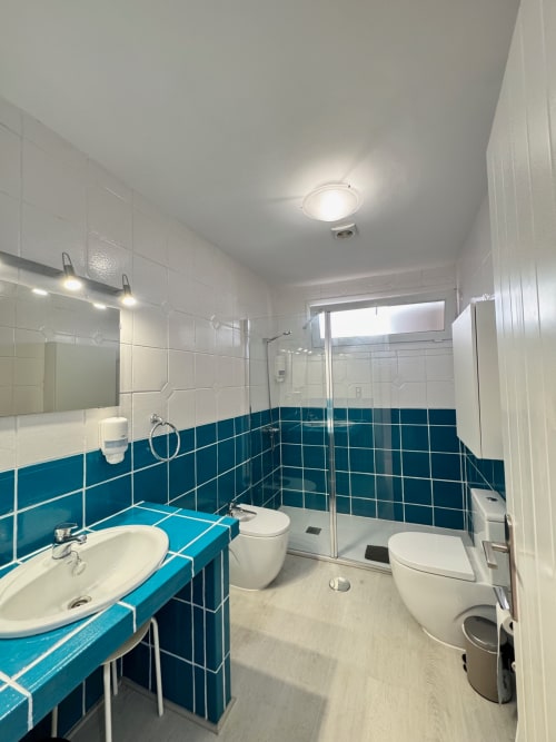 Baño moderno con azulejos turquesa y blanco, lavamanos, inodoro, ducha y espejo en El Faro De Los Genoveses, San José