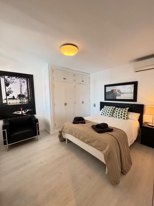 Moderno dormitorio en El Faro De Los Genoveses con cama de matrimonio, TV de pantalla plana, armario, butaca negra y luz cálida en el techo