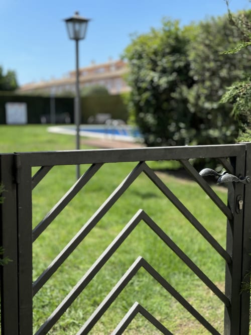 Puerta decorativa negra que abre a un jardín cuidado con piscina, farola y setos en la casa de alquiler La Vela de Estartit