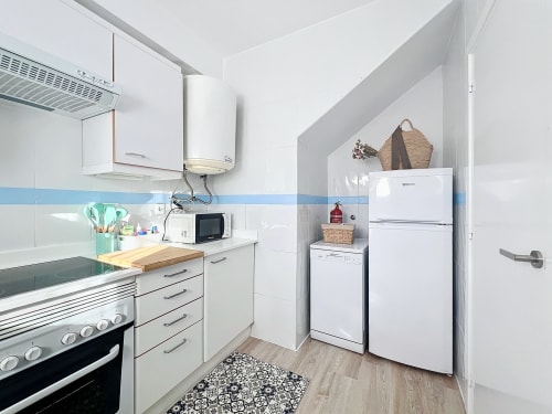 Cocina moderna y luminosa en la casita La Vela de Estartit Rental, con armarios blancos, electrodomésticos de acero inoxidable y azulejos azules