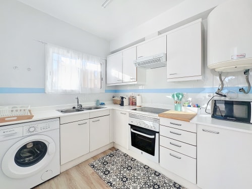 Cocina moderna y blanca en la casa rural La Vela de Estartit, con lavadora, horno y azulejos azules