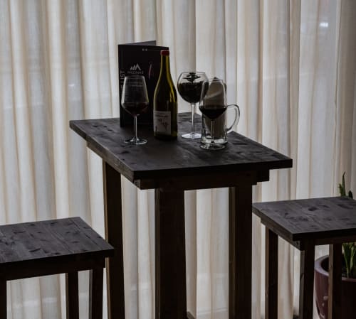 Bar dell'Hotel Milomax con bottiglia di vino, bicchieri di vino rosso e tavoli in legno nero davanti a tende bianche