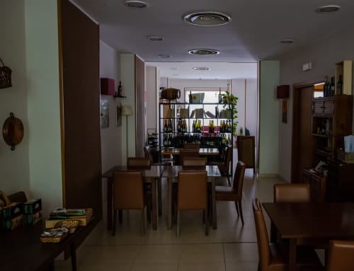 Area ristorazione dell'Hotel Milomax con tavoli in legno, sedie e scaffali che espongono bottiglie a Milo, Italia
