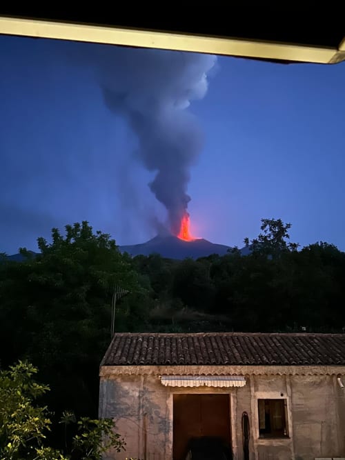Eruzione vulcanica notturna vista dall'Hotel Milomax a Milo, Sicilia con colata lavica e pennacchio di cenere