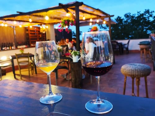 Zwei Weingläser bei Sonnenuntergang auf der Dachterrasse des Hotel Milomax in Milo, mit Pergola und Gästen im Hintergrund
