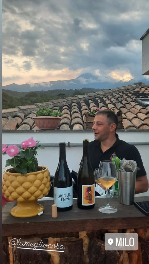 Uomo che assapora vino sulla terrazza dell'Hotel Milomax a Milo, Sicilia, con vista sul vulcano e tetto in coppi