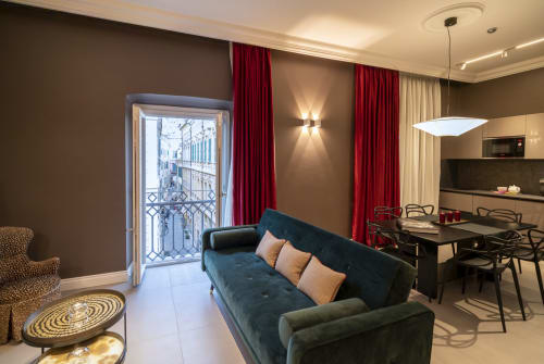 Suite moderna alle Seven Suites Sanremo con divano teal scuro, tende rosse, vista sul balcone e zona cucina open space