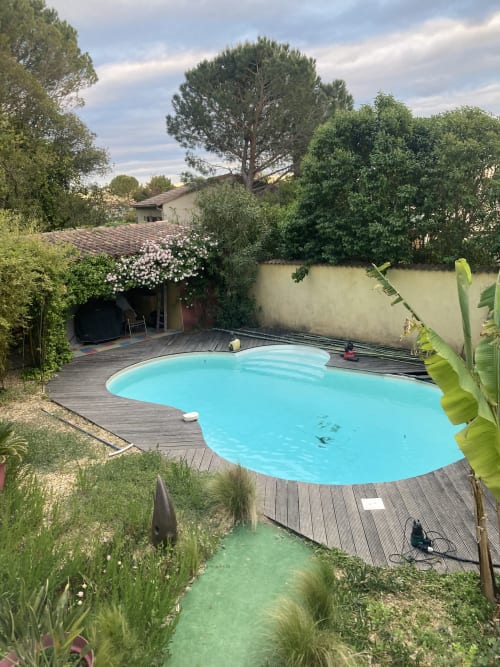 Turquoise pool with wooden deck surrounded by lush gardens at La Conciergerie De Franck villa in Boissieres