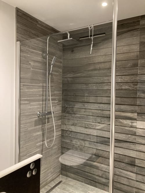 Modern shower enclosure with wood-grain tiling at La Conciergerie De Franck villa in Boissieres, France