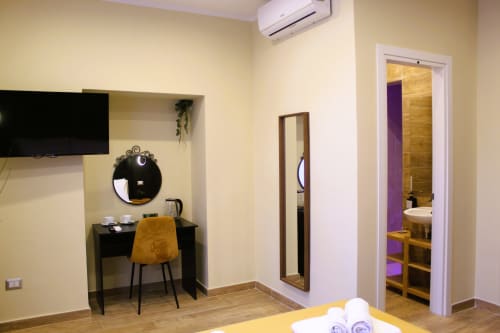 Camera moderna di Blackwoody Contemporary Hospitality Napoli con scrivania nera, specchio rotondo, sedia gialla e bagno