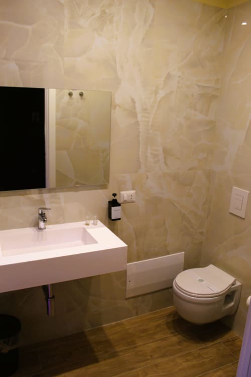 Bagno moderno con lavabo bianco, water sospeso, rivestimento in marmo e specchio presso Blackwoody Contemporary Hospitality