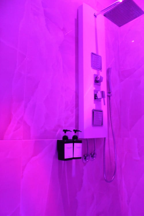 Bagno moderno con illuminazione neon viola, zona doccia e accessori a parete presso Blackwoody Contemporary Hospitality, Napoli