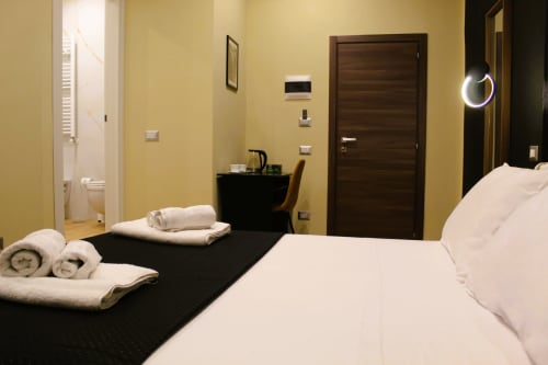 Camera moderna al Blackwoody Contemporary Hospitality di Napoli con biancheria bianca, scrivania scura, pareti gialle e bagno privato