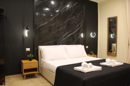 Camera moderna a Blackwoody Contemporary Hospitality a Napoli con parete in marmo, biancheria bianca e asciugamani arrotolati.
