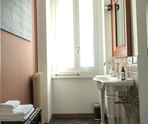 Elegante bagno a Porta Tosa Milano con lavabo su colonna, radiatore vintage, luce naturale e finiture classiche