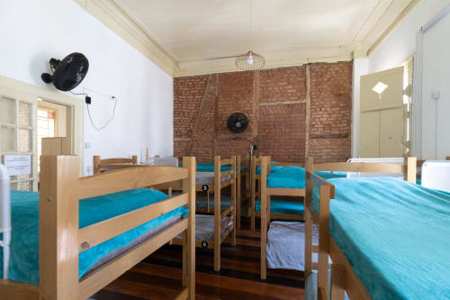 Mixed dormitory room at Rio Vibes Hostel with wooden bunk beds, turquoise bedding, exposed brick walls, and wooden flooring