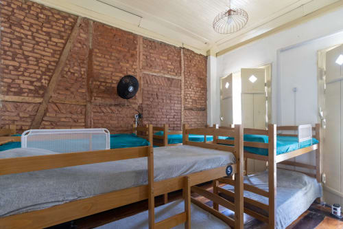 Dormitório misto do Rio Vibes Hostel com beliche de madeira, colchões azuis, paredes de tijolos e ventilador de teto no Rio de