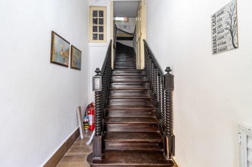 Escada de madeira escura no Rio Vibes Hostel no Rio de Janeiro levando aos dormitórios do andar superior com corrimãos e paredes brancas