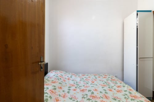 Quarto brilhante no Rio Vibes com roupa de cama floral, porta de madeira, guarda-roupa branco e paredes brancas