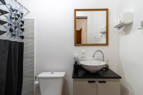 Banheiro moderno da Rio Vibes Hostel Suite no Rio de Janeiro com pia redonda branca, espelho de madeira, vaso sanitário e área de chuveiro