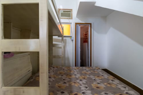 Quarto triplo Rio Vibes Hostel com piso de azulejos florais, guarda-roupa embutido, ar condicionado de janela e portas de madeira marrom