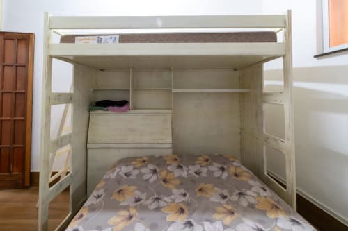 Cream-colored loft bed with floral bedding at Rio Vibes Hostel in Rio de Janeiro, featuring storage and shelving.