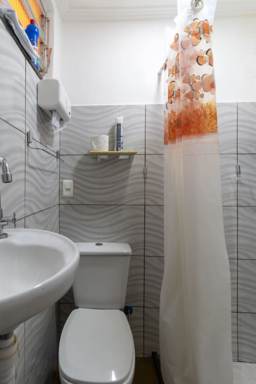 Banheiro moderno na Rio Vibes Hostel com pia branca redonda, vaso sanitário, box de chuveiro de vidro e paredes com azulejos ondulados