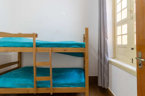 Literas de madera con ropa de cama turquesa en una habitación del albergue Rio Vibes, Río de Janeiro, con paredes y puerta blancas