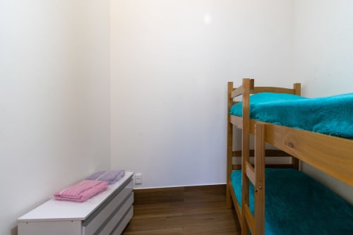 Dormitório de albergue com beliches de madeira, roupa de cama em tons de turquesa e cama individual com almofadas rosa no Rio Vibes Hostel, Rio de