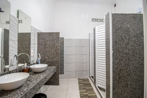 Banheiro compartilhado moderno no Rio Vibes Hostel no Rio de Janeiro com duas pias, balcões de granito e chuveiro azulejade