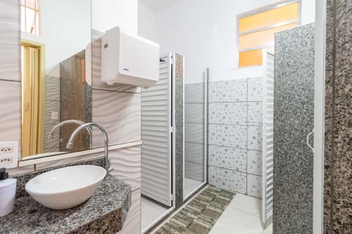 Banheiro compartilhado moderno na pousada Rio Vibes no Rio de Janeiro com pia dupla, chuveiro walk-in e acabamentos em pedra
