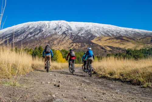 Trois cyclistes sur un sentier de montagne avec un volcan enneigé et des prairies dorées près de l'Hôtel Milomax à Milo, Sicile