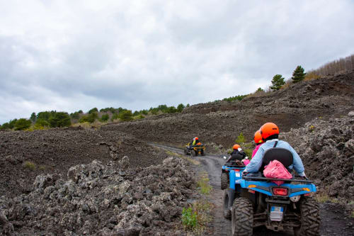 Motocyclistes en VTT sur terrain volcanique près de l'Hôtel Milomax à Milo, Sicile, avec paysage de lave et forêt en arrière-plan