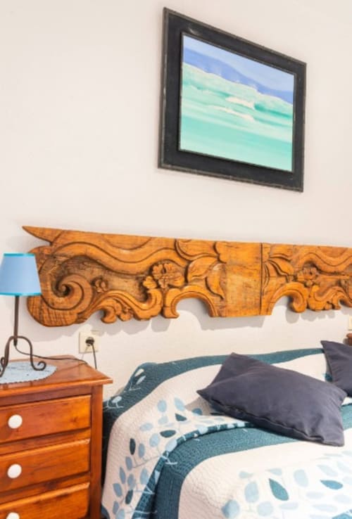 Acogedora habitación en Can Gat Vell B&B en Girona con cabecero de madera tallada, ropa de cama azul y cuadro de paisaje enmarcado