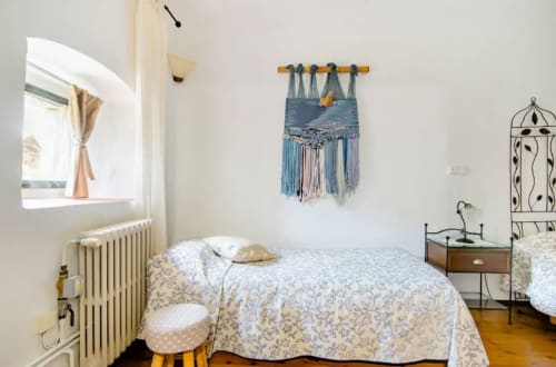 Dormitorio luminoso en Can Gat Vell en Girona con ropa de cama estampada, radiador y decoración mural bohemia.