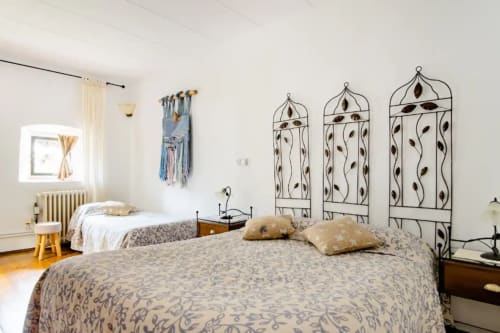 Habitación de huéspedes en Can Gat Vell B&B en Girona con dos camas, cabeceros de hierro forjado y adornos decorativos en las paredes.