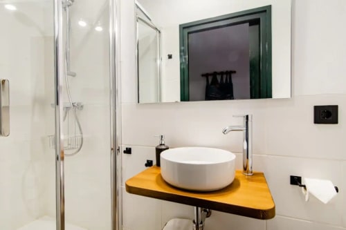 Baño moderno en Can Gat Vell con lavabo de cerámica blanca sobre encimera de madera amarilla, espejo y ducha de cristal en Girona