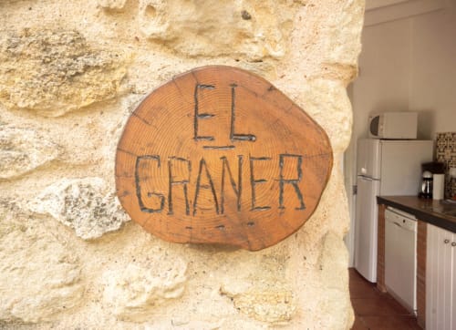 Letrero de madera 'El Graner' en muro de piedra de Can Gat Vell, casa rural en Girona, Cataluña