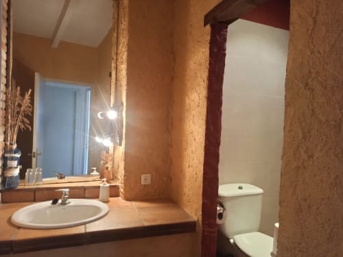 Baño de la casa rural Can Gat Vell en Girona con paredes de corcho, lavabo, inodoro y espejo iluminado