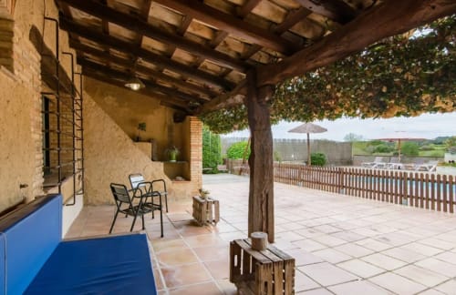 Patio cubierto del B&B Can Gat Vell en Girona, España, con asientos, vigas de madera y vistas al campo