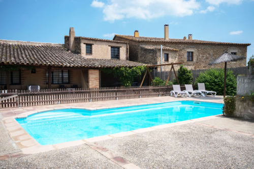 Piscina Can Gat Vell y edificios de piedra en Empordà, Girona, Cataluña con tumbonas y patio