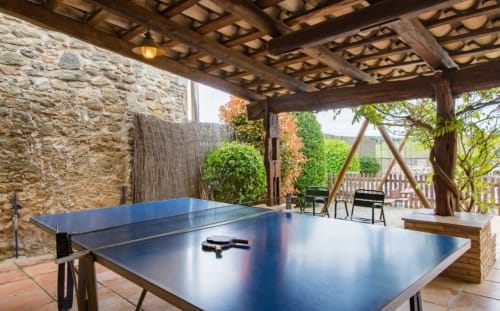 Mesa de ping-pong azul bajo pérgola de madera en Can Gat Vell, casa rural en Girona con arquitectura de piedra