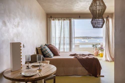 Dormitorio costero luminoso en Formentera Especial con vistas al mar, ropa de cama marrón, lámpara colgante tejida y mesa comedor redonda en La