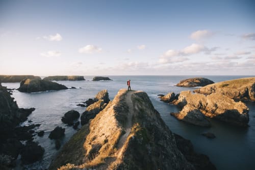 Personne debout sur une falaise rocheuse surplombant les eaux turquoise et les îles de Belle-Île-en-Mer, Bretagne
