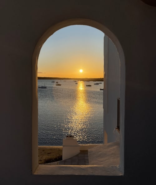 Vista del atardecer a través de un arco en Formentera Especial, La Savina, con barcas amarradas y reflejos dorados en el agua